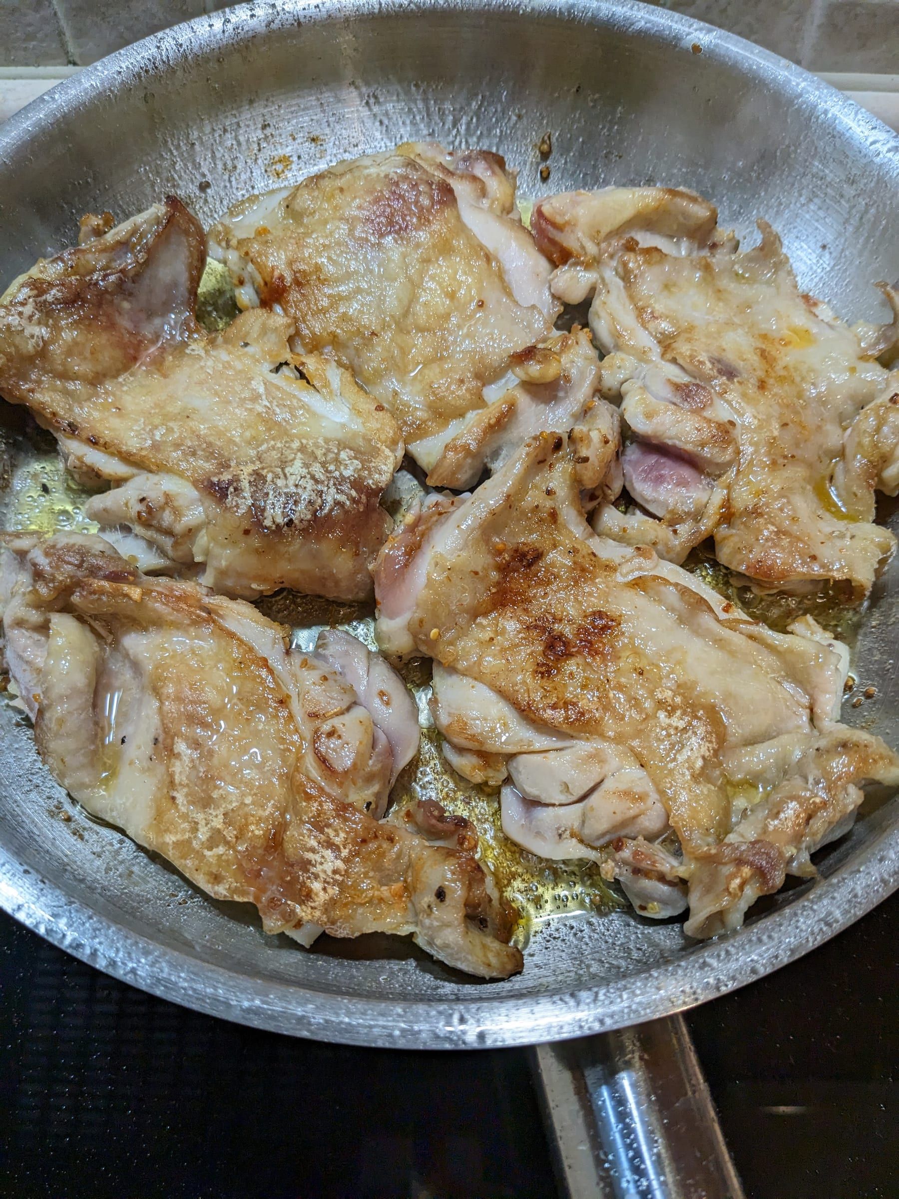 Куриные бёдра кожей вверх с золотистой корочкой на стальной сковороде